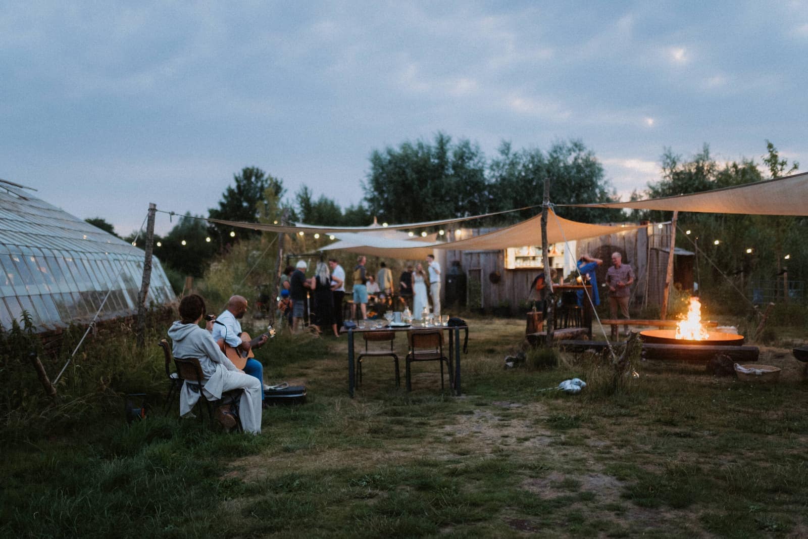 Abendliche Atmosphäre bei einer Outdoor-Hochzeit im Garten mit Feuerstelle, Lichterketten und Live-Musik.