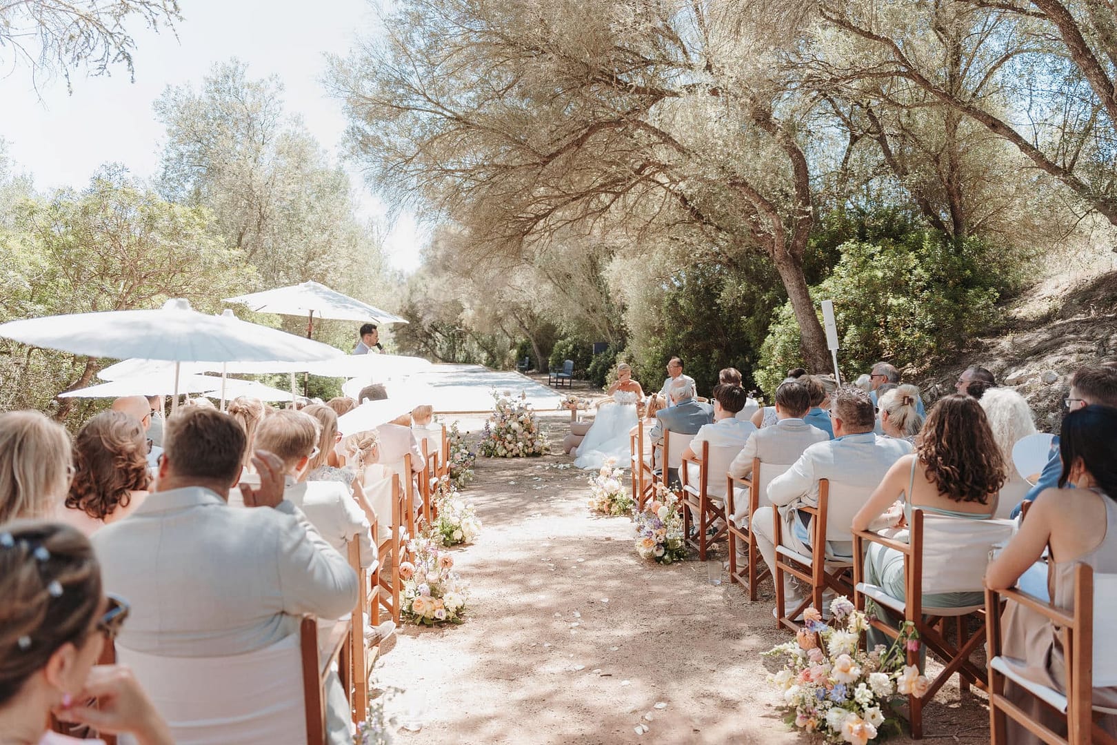 Hochzeitszeremonie unter freiem Himmel mit Gästen und floraler Gestaltung und Sonnenschirmen