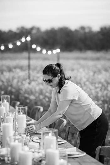 Weddingplanner bereitet einen Tisch für ein Outdoor-Hochzeitsevent mit Kerzen und Lichterkette vor