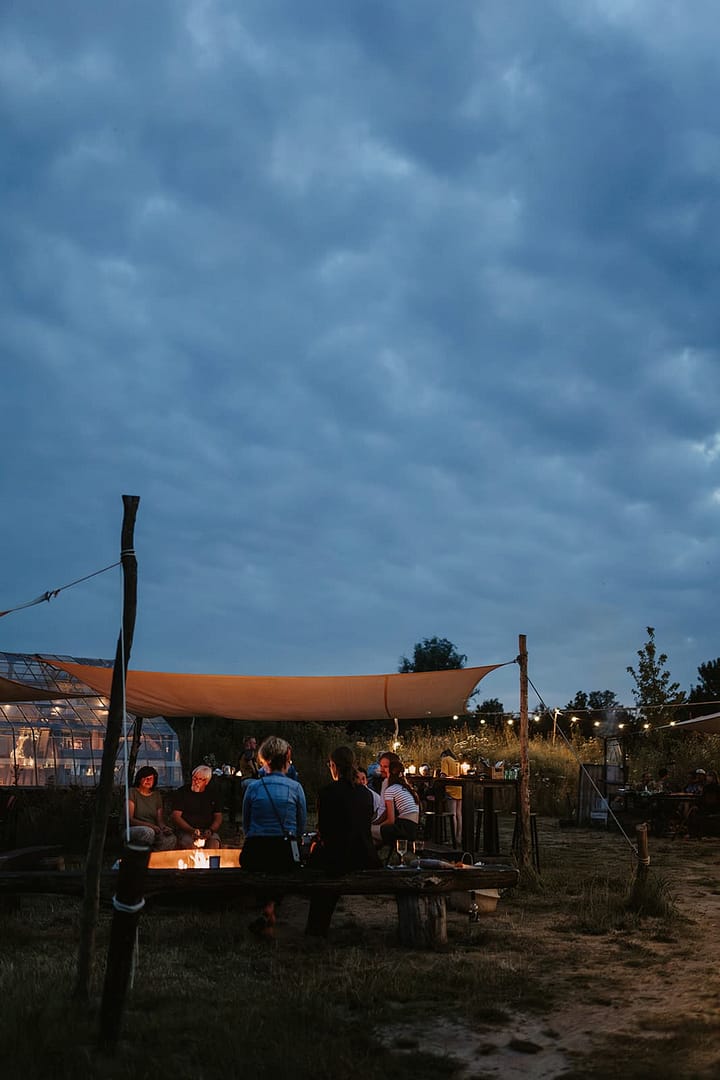Gäste sitzen am Abend gemeinsam am Feuer unter freiem Himmel