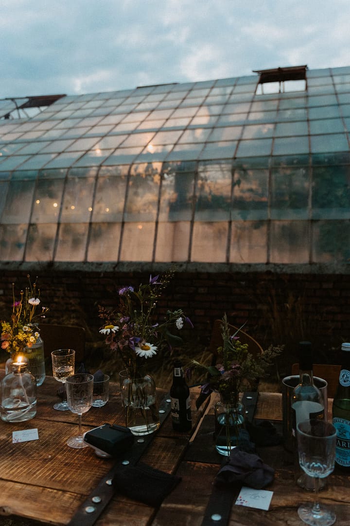 Lange Tafel unter freiem Himmel bei einer Outdoor-Hochzeit mit Gewächshaus im Hintergrund, geplant durch einen Hochzeitsplaner