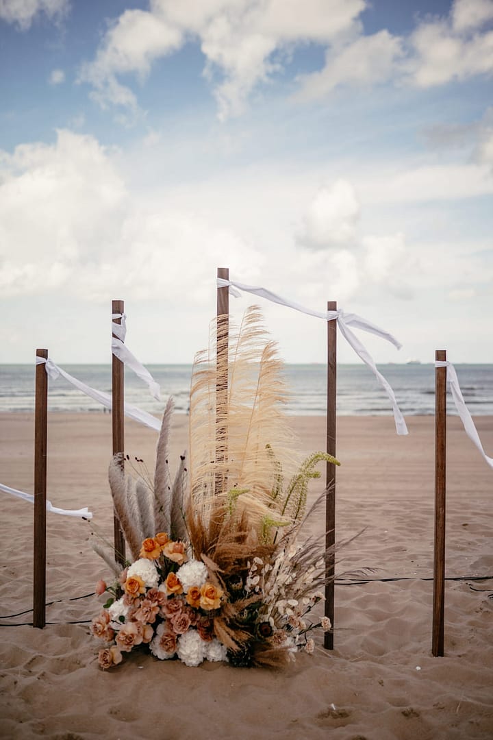 Trauung am Strand in Holland mit Holzbogen, Blumenarrangement und Blick auf das Meer