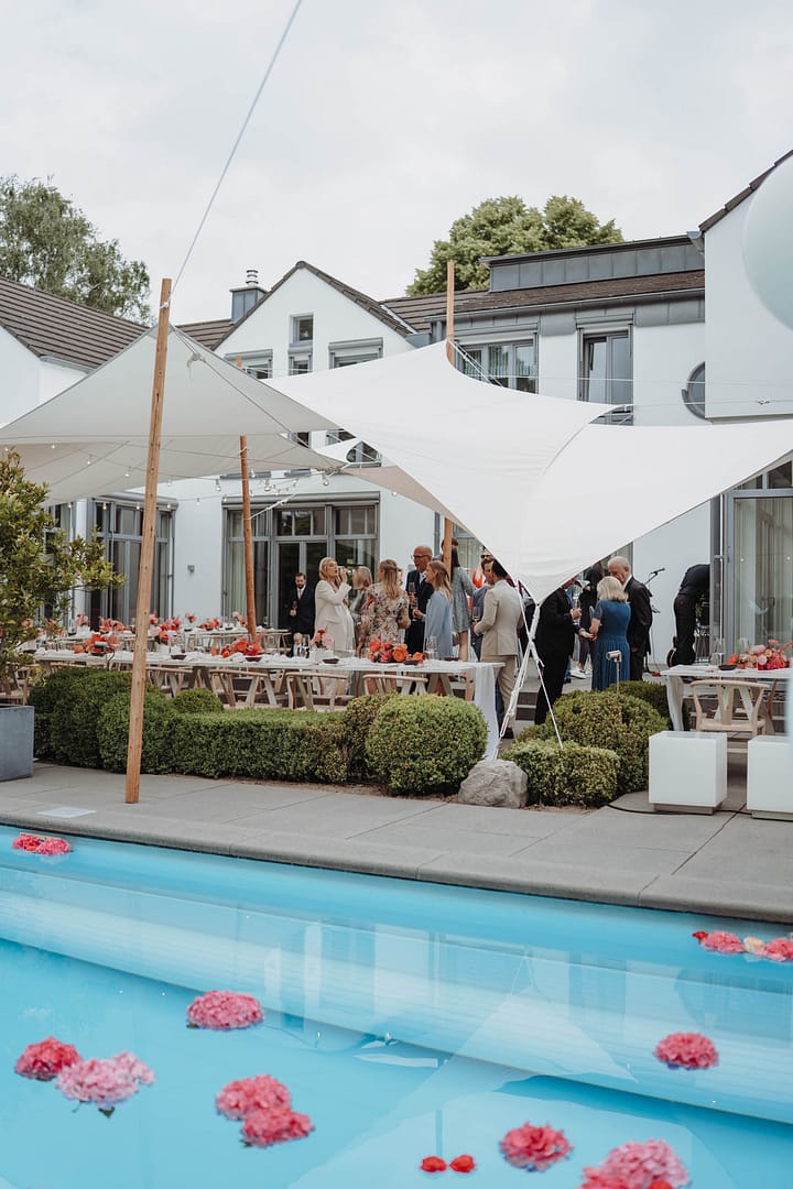Gesamtansicht einer Zelthochzeit im Garten eines privaten Anwesens mit Stretchzelt und langen Tafeln und Pool