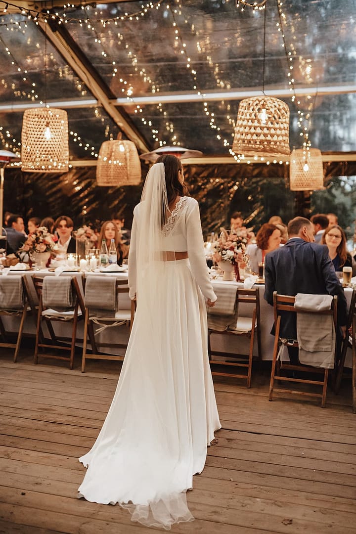 Braut steht am Kopf einer langen Tafel unter dem Zelt bei einer Outdoor Hochzeit im Rahmen eines Wedding Weekends