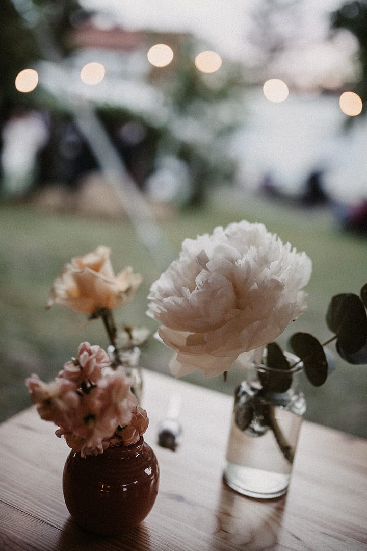 Florales Tischdetail mit Kerzen und Pfingstrosen bei einer Outdoor-Hochzeit an einem stilvollen Ferienhaus.