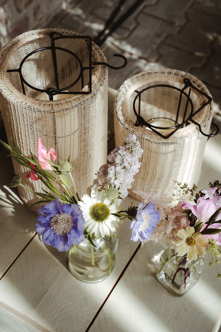 Florale Detailaufnahme mit Windlichtern und Sommerblumen auf Holztisch – natürliche Dekoration im Rahmen einer hochwertig geplanten Zelthochzeit.