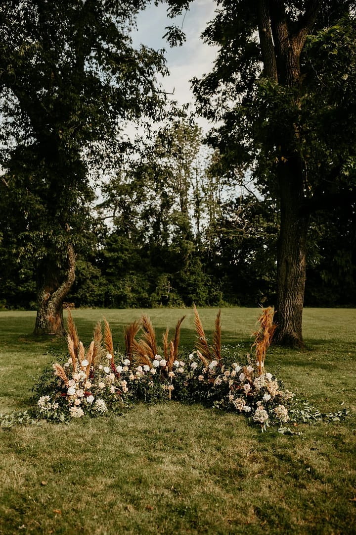 Freie Trauung im Garten mit floralem Backtrop, umgesetzt für eine Hochzeit im eigenen Zuhause oder Ferienhaus.