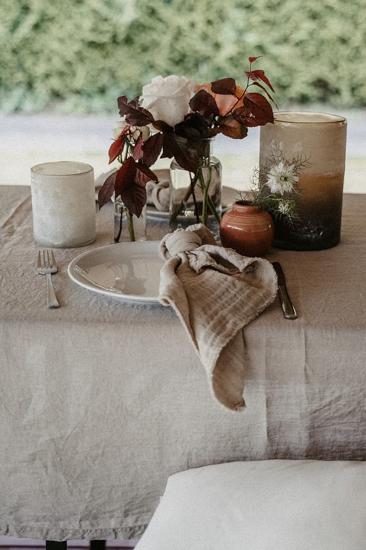 Natürliches Tischdekodetail mit Leinen, Kerzen und floralen Akzenten für eine Gartenhochzeit im eigenen Zuhause oder Ferienhaus.