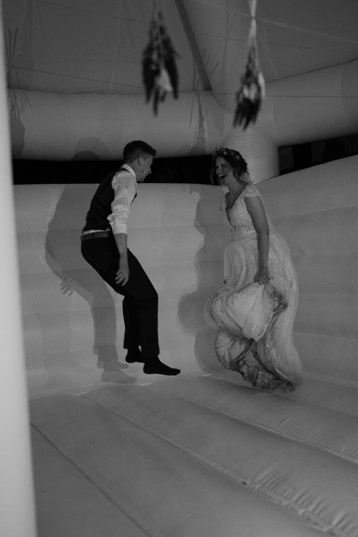 Ausgelassene Feiermomente mit viel Bewegung und Leichtigkeit auf einer weissen Hüpfburg für Hochzeiten als Teil eines ungezwungenen Hochzeitswochenendes in einer Off-Location im Wald.