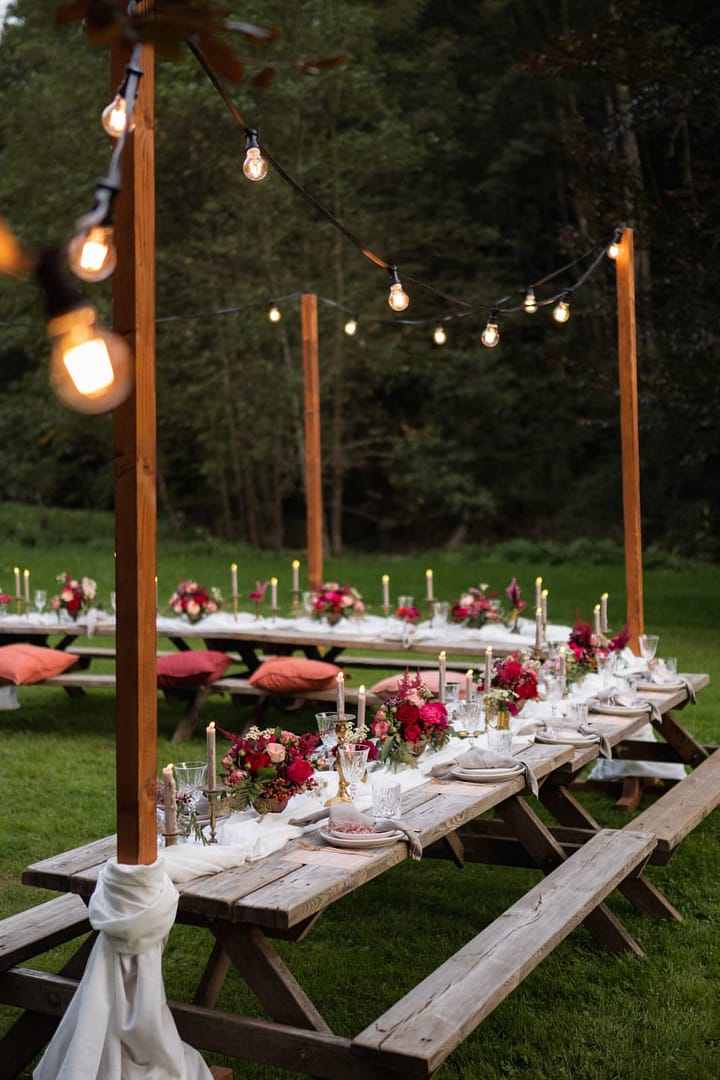 Lange Holztafeln im Picknick Style unter Lichterketten als gemeinsames Dinner bei einem entspannten Outdoor Wedding-Weekend.