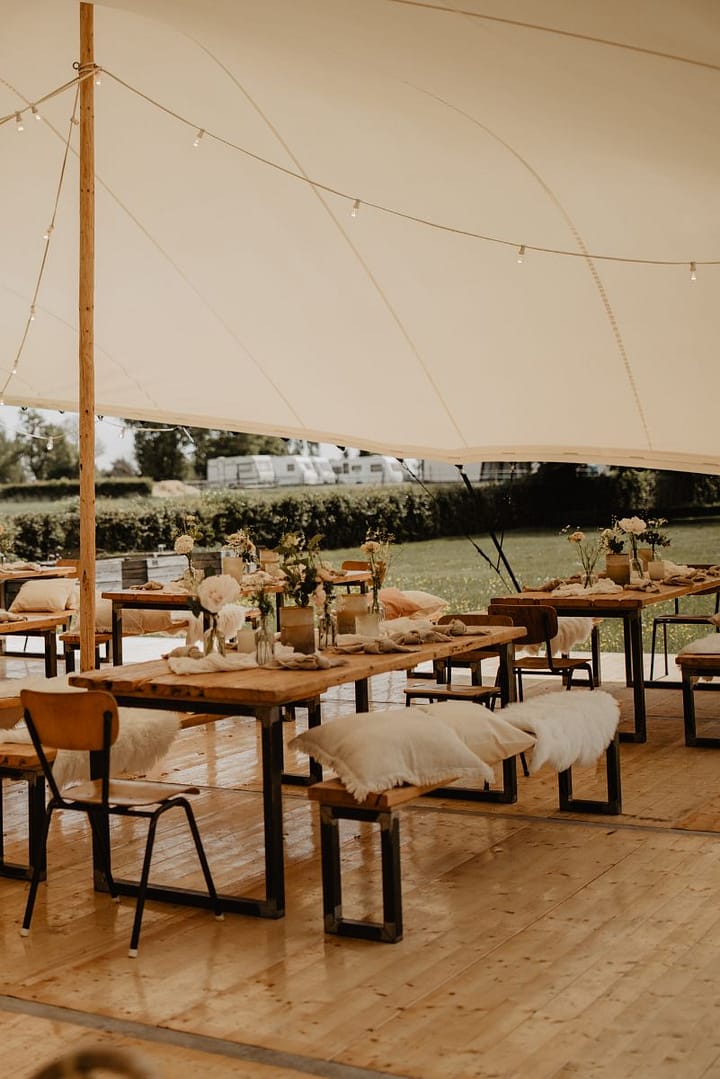 Lange Tafeln unter einem Stretchzelt bei einer Outdoor-Hochzeit mit natürlichem, reduziertem Design im Scandi-Style