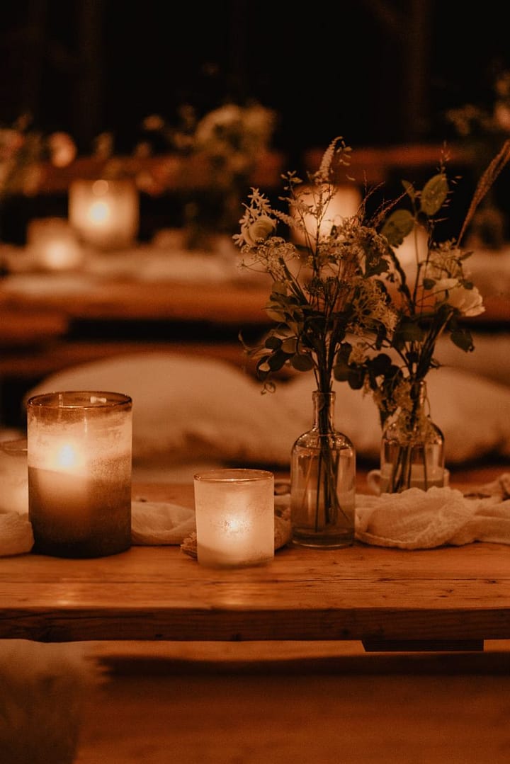 Kerzenlicht und florale Tischdekoration im skandinavischen Design sorgen für warme Abendstimmung bei einer Outdoor-Hochzeitsfeier.