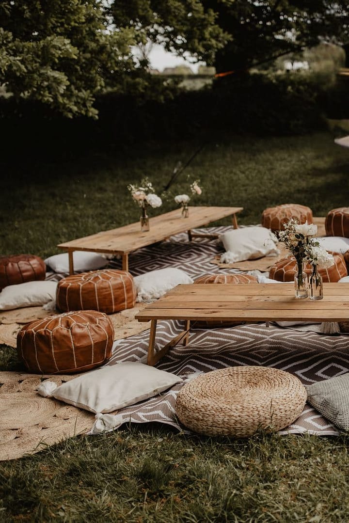 Lounge-Bereich mit niedrigen Holztischen, Kissen und Teppichen für Gäste bei einem entspannten Outdoor-Picknick.