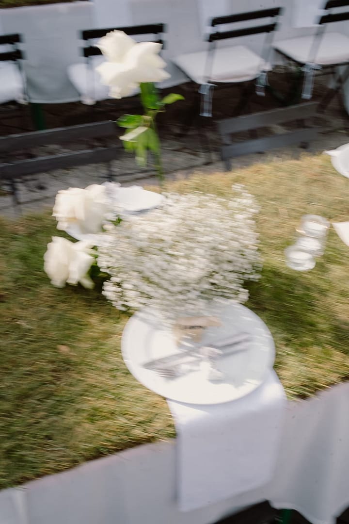Bewegtes Tischdetail mit floralen Elementen bei einer Outdoor-Hochzeit, eingefangen zwischen Struktur und Lebendigkeit.