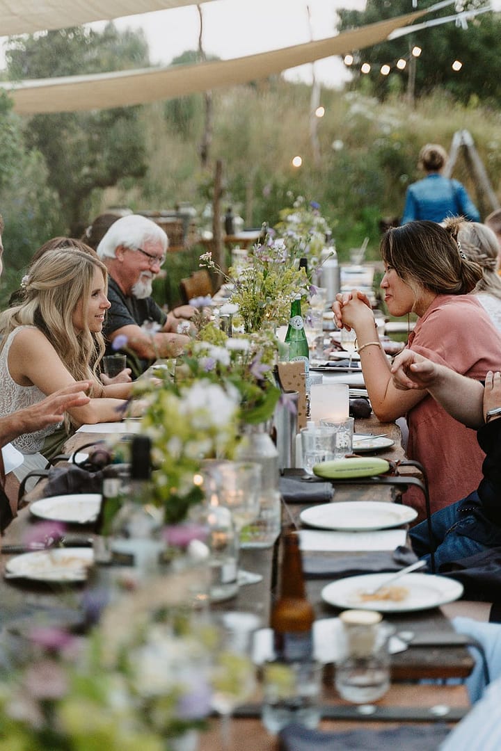 Gäste sitzen bei einem gemeinsamen Dinner an einer langen Tafel im Freien – ein Moment, der die Philosophie der Hochzeitsplanung mit Atmosphäre, Gemeinschaft und entspanntem Feiern widerspiegelt.