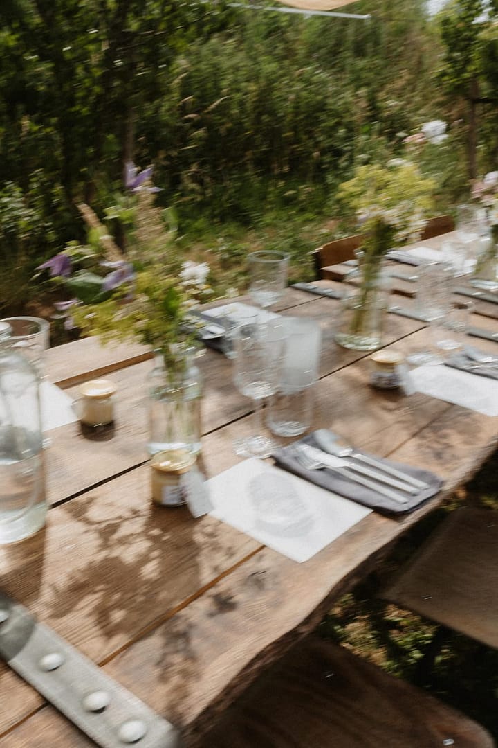 Lange Holztafel für ein gemeinsames Dinner bei einer Outdoor-Hochzeit im Garten mit natürlicher Tischdekoration aus Wildflowers und Wiesenblumen.