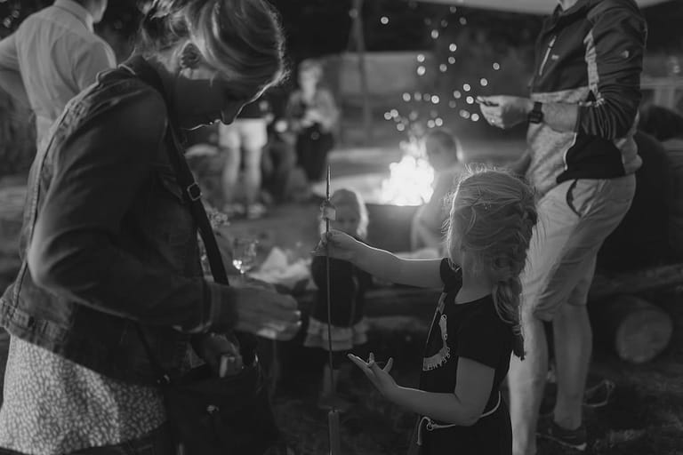 Kind und Erwachsene beim gemeinsamen Lagerfeuer-Moment – familiäre und emotionale Stimmung eines Hochzeitswochenendes in Schwarz-Weiß