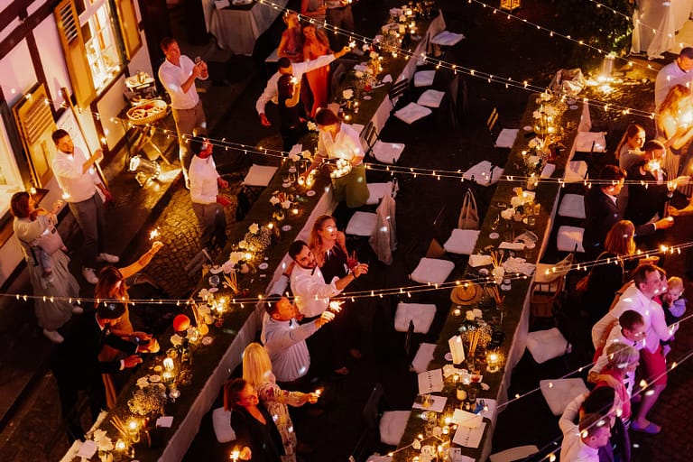 Lange Tafeln aus der Vogelperspektive bei einer Outdoor-Hochzeit, begleitet von warmem Licht und lebendiger Atmosphäre.