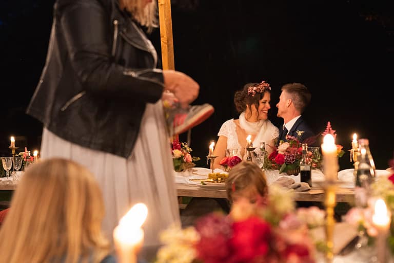 Brautpaar genießt das gemeinsame Dinner bei Kerzenlicht während eines entspannten Outdoor-Hochzeitswochenendes.
