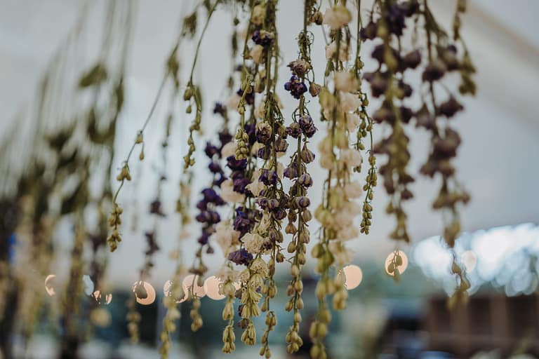 Hängende Blumeninstallation aus Rittersporn unter einem Zelt bei einer Outdoor-Hochzeit im Schlosspark, umgesetzt im Rahmen einer ganzheitlichen Hochzeitsplanung und Eventplanung.