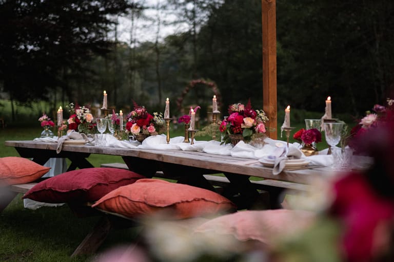 Lange Tafel unter freiem Himmel mit Kerzen, floraler Tischdekoration und Sitzkissen – stimmungsvolles Dinner bei einer Outdoor Hochzeit in einem AirBnB in Belgien.