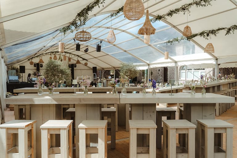 Offener Blick durch das Hochzeitszelt auf Bar- und Aufenthaltsbereiche eines exklusiven Wedding Weekends auf privatem Anwesen, vollständig geplant und koordiniert.