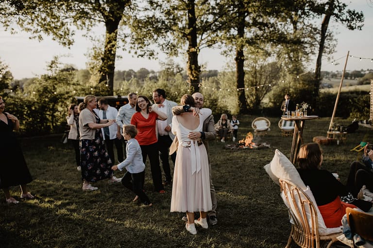 Gäste tanzen und umarmen sich bei einer Outdoor-Hochzeit in stimmungsvoller Dämmerung am Lagerfeuer.
