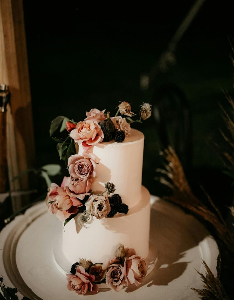 Hochzeitstorte mit floralen Akzenten als Abenddetail bei einer Outdoor-Hochzeit an einem privaten Ferienhaus.