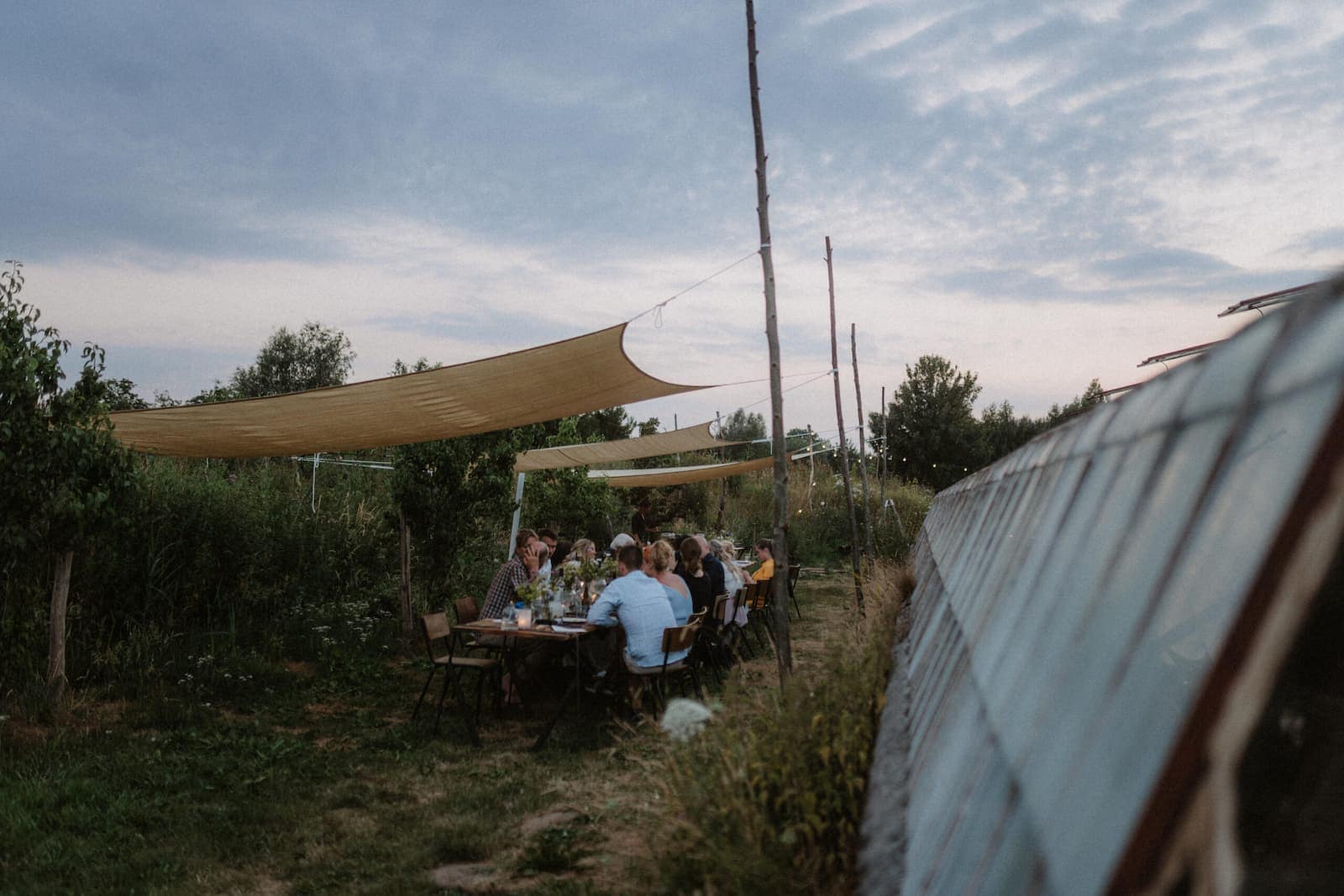 Gäste sitzen an einer langen Tafel unter Sonnensegeln im Freien