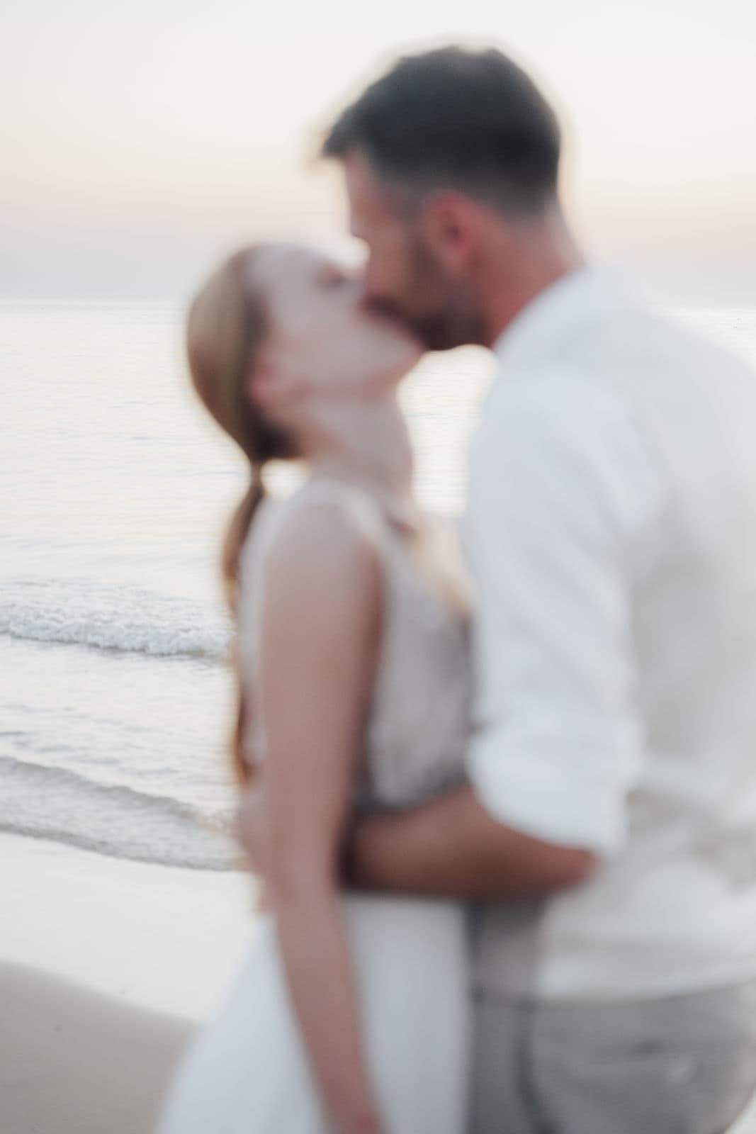 Brautpaar küsst sich am Strand während einer Hochzeitsfeier im Abendlicht