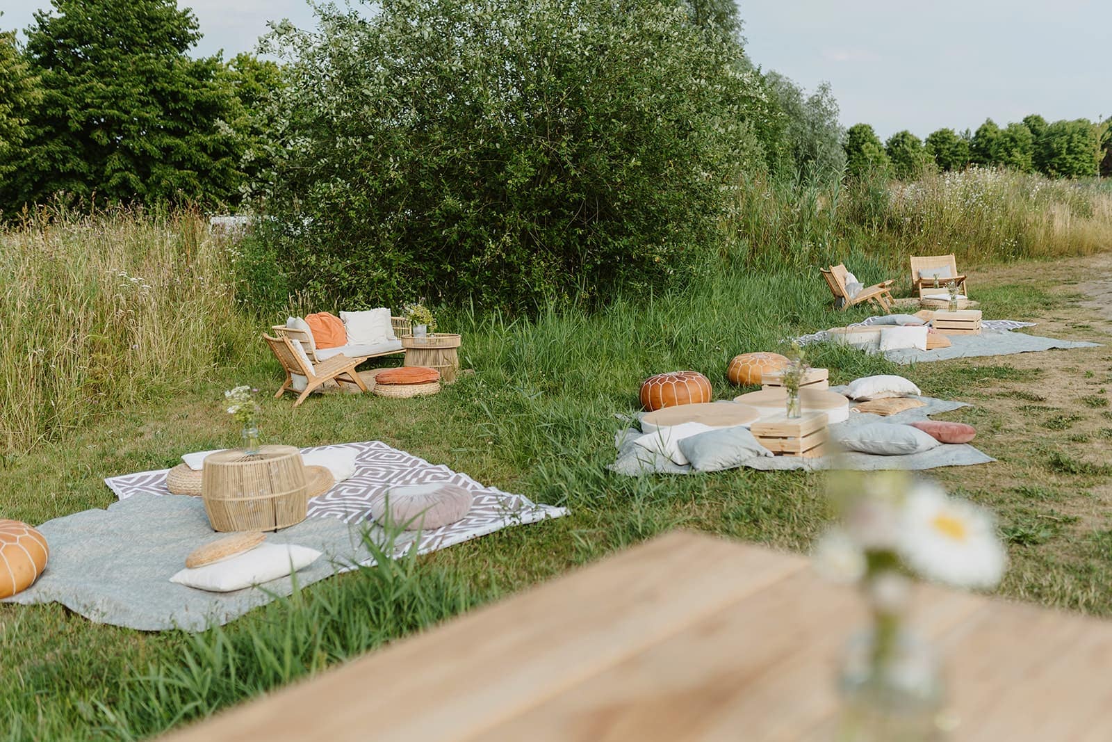Lounge- und Picknickbereich auf einer Wiese mit Kissen und Holzmöbeln bei einer Outdoor Wedding