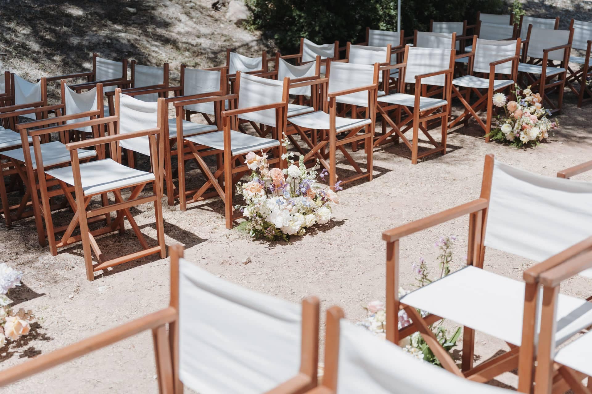 Stuhlreihen mit floralen Arrangements für eine Trauung unter freiem Himmel